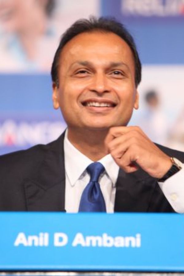 Anil Ambani speaking at a business event with Reliance ADA Group logo in the background.